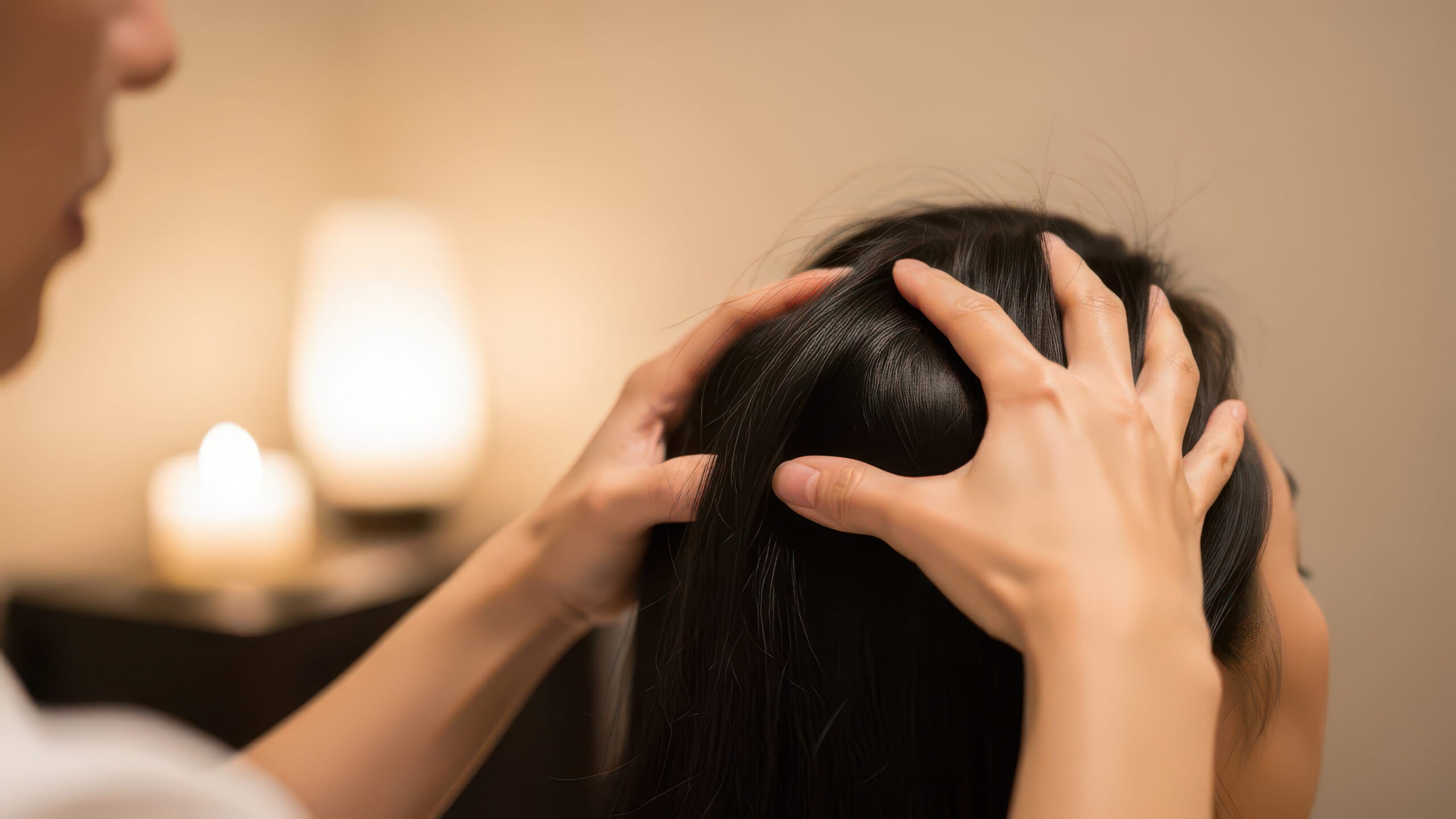 A close up of a massage therapists hands on a brunette womens head massaging