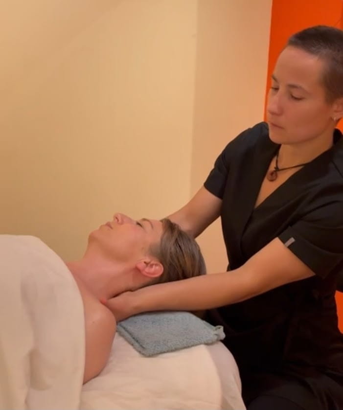 Massage therapist massaging a clients neck as they are lay down with a towel across them